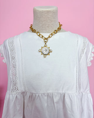 White dress with gold chain necklace on a mannequin against a pink background