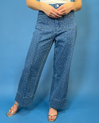 A person wearing blue wide-leg denim pants with a white polka-dot pattern, paired with a white top and metallic sandals