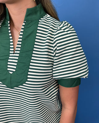 A close-up of a woman wearing a short-sleeve top with dark green and white horizontal stripes, featuring a solid dark green collar and placket