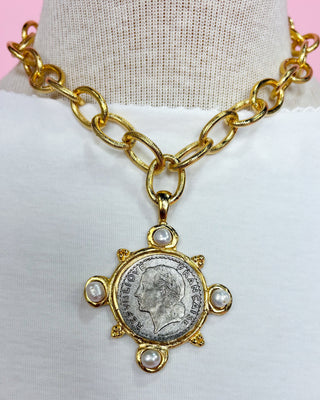 Gold chain necklace with a coin pendant on a mannequin bust against a pink background