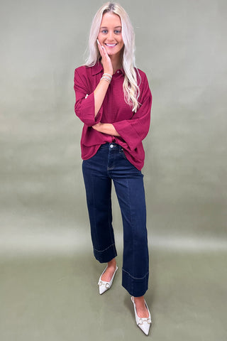 Woman wearing a burgundy shirt and blue jeans against a plain background