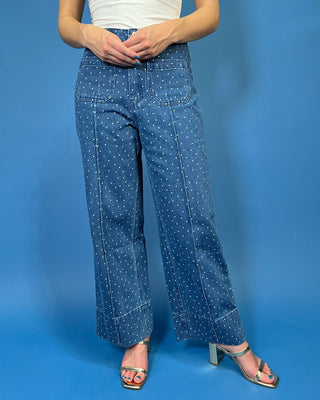 A person wearing blue wide-leg denim pants with a small white polka dot pattern, styled with a white top
