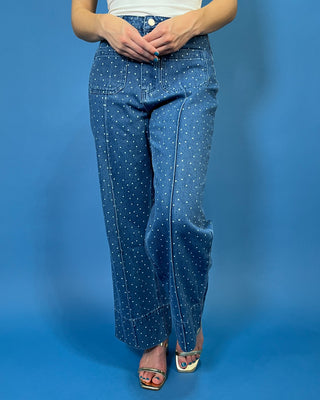 A person wearing blue denim jeans with a white polka-dot pattern, paired with a white top and metallic sandals