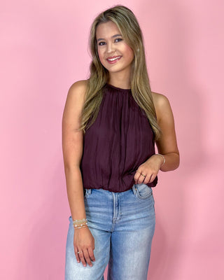 Woman wearing a purple top and blue jeans against a pink background