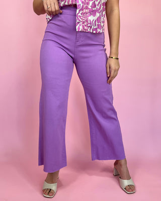 Person wearing purple pants and a patterned top on a pink background