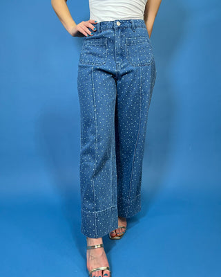 A person modeling a pair of wide-leg blue denim jeans with a small white polka dot pattern, paired with a white top and metallic sandals