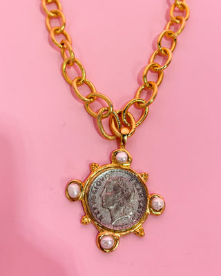 Gold necklace with a coin pendant on a pink background