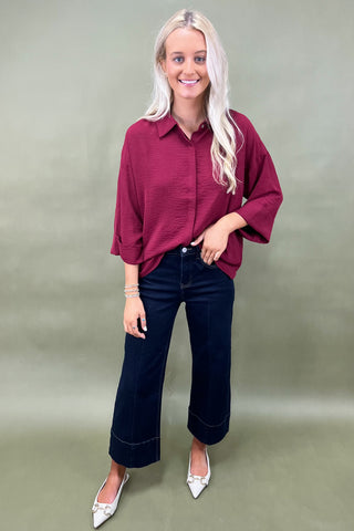 Woman wearing a burgundy shirt and blue jeans against a plain background