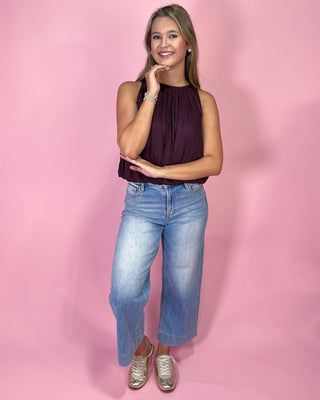 Woman wearing a purple top and blue jeans against a pink background