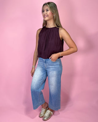 Woman wearing a sleeveless purple top and blue jeans against a pink background