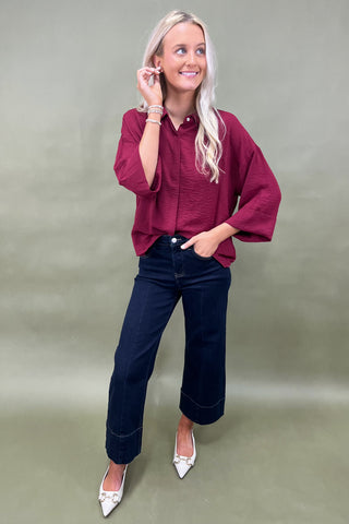 Woman wearing a burgundy shirt and blue jeans against a plain background