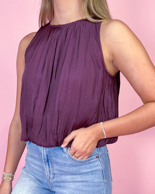 Person wearing a purple sleeveless top and blue jeans against a pink background