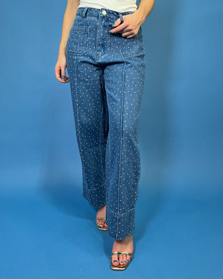 A person modeling a pair of wide-leg blue jeans with a white polka-dot pattern, paired with a white top and metallic sandals