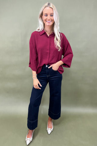 Woman wearing a burgundy shirt and blue jeans against a plain background