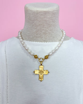Pearl necklace with a gold cross pendant on a mannequin against a pink background
