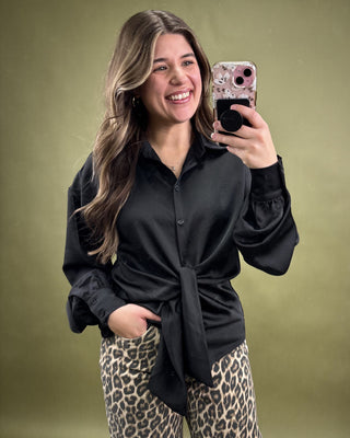 Woman taking a selfie wearing a black top and leopard print pants on a green background