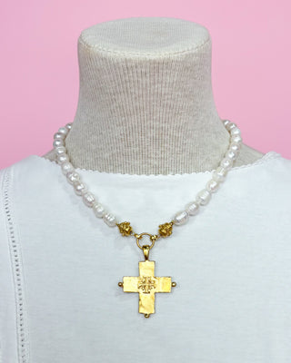 Pearl necklace with a gold cross pendant on a mannequin against a pink background