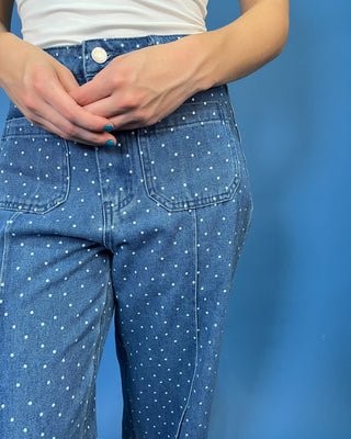 Close-up of a person wearing blue denim jeans with a white polka dot pattern, paired with a white top