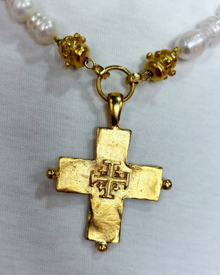 Gold cross pendant on a pearl necklace against a white background