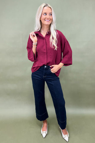 Woman wearing a burgundy shirt and blue jeans against a plain background