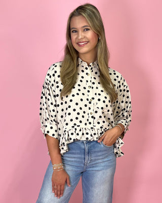 Woman wearing a polka dot blouse and jeans against a pink background