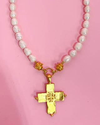Necklace with pink beads and a gold cross pendant on a pink background