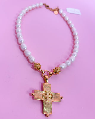 Pearl necklace with a gold cross pendant on a pink background