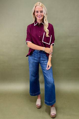 Woman wearing a burgundy shirt with white trim and blue jeans on a green background