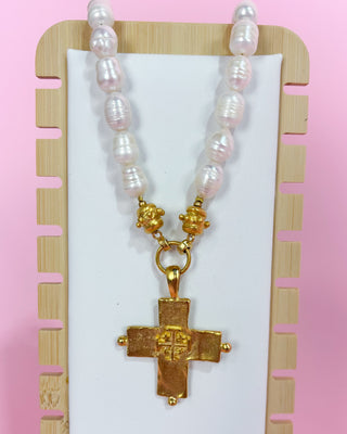 Pearl necklace with gold cross pendant on a pink background