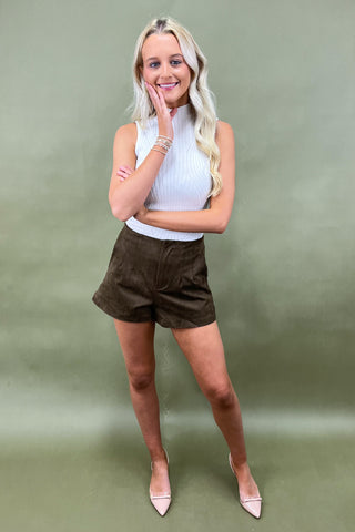 Woman wearing a white top and brown shorts against a green background