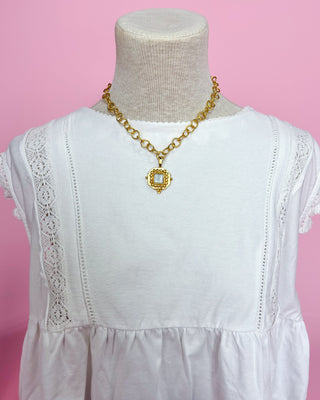 White dress with gold necklace on a mannequin against a pink background