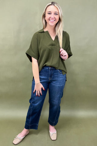 Woman wearing an olive green top and blue jeans against a green background