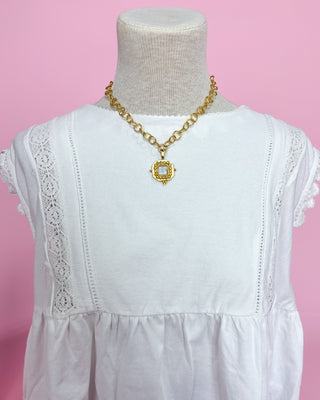 White dress with gold necklace on a mannequin against a pink background