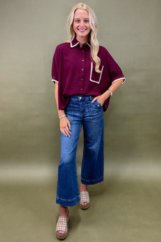 Woman wearing a maroon shirt and blue jeans against a green background