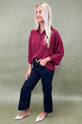 Woman wearing a burgundy shirt and blue jeans against a plain background