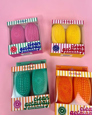 Four packages of cleaning brushes with colorful packaging on a pink background