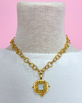 Gold chain necklace with a pendant on a mannequin against a pink background