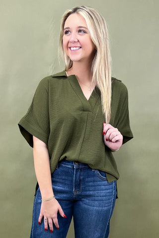 Woman wearing an olive green top and blue jeans against a green background