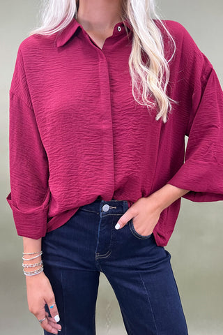 Woman wearing a burgundy shirt and blue jeans against a plain background