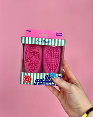 Pink grooming brushes in packaging held against a pink background