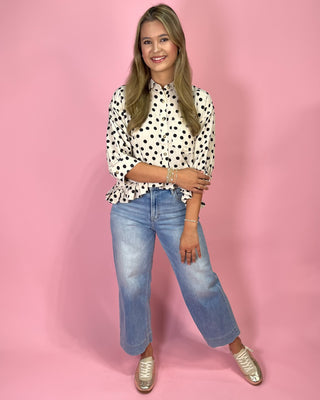 Woman wearing a polka dot blouse and jeans against a pink background