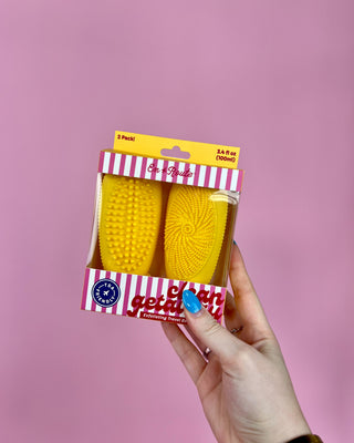 Hand holding a package of yellow silicone scrubbers with a pink background