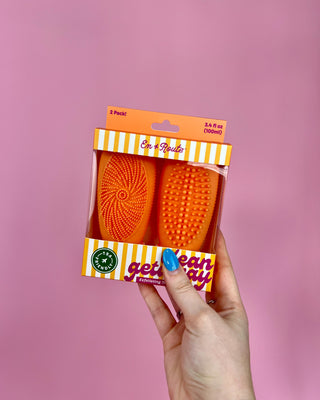 Hand holding a package of orange cleaning brushes with a pink background