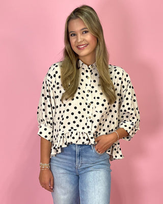 Woman wearing a polka dot blouse and jeans against a pink background