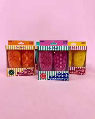 Three packages of cleaning brushes with colorful packaging on a pink background