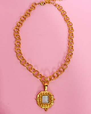 Gold chain necklace with a pendant on a pink background