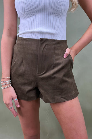 Person wearing brown suede shorts and a light blue top against a neutral background