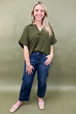 Woman wearing an olive green top and blue jeans against a green background
