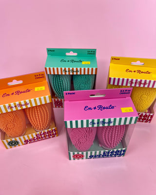Four boxes of 'En Route' products on a pink background