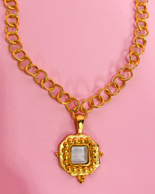 Gold necklace with a pendant on a pink background